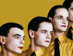 Uma releitura artística da icônica imagem da banda Kraftwerk, apresentando quatro homens em uma composição diagonal. Eles possuem pele muito clara, cabelos escuros penteados para trás e lábios pintados com batom vermelho vibrante. Todos vestem camisas de um tom amarelo-ouro cintilante com gravatas pretas finas, posicionados contra um fundo sólido também na cor amarelo-ouro. O estilo visual remete à estética retrô-futurista e minimalista do grupo original.